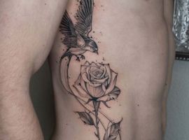 Вражаюча тату-робота з птахом і рожевою квіткою на боці клієнта. Троянда і птах