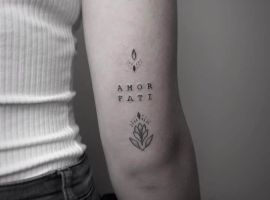 Маленькое тату "Amor Fati" с цветочным орнаментом на предплечье, символизирующее принятие судьбы и любовь к жизни. Тату "Amor Fati" на руке с цветочным дизайном, выполненное в стиле минимализм.