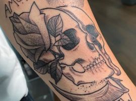 Мистецьке татуювання "Amor Fati" з черепом, квітами та листям, що символізує прийняття долі та життєвий філософський підхід. Татуювання черепа з квітами та листям, символ "Amor Fati".