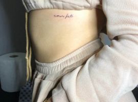 Модель з татуюванням "Amor Fati" на животі, що символізує прийняття долі та життєвих випробувань. Татуювання "Amor Fati" на боці живота, символ прийняття долі та життєвого шляху.
