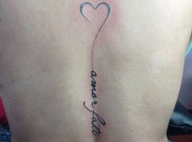 Малюнок тату з сердечком і фразою "amour fati" на боці, символізує прийняття долі та любов до життя. Тату з сердечком і написом "amour fati" на боці.