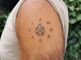 Стильне тату з вогнем і фразою "Amor Fati" на руці, що символізує прийняття життєвих випробувань. Тату з вогнем і словами "Amor Fati" на руці, символ прийняття долі.