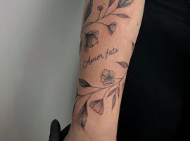 Модне тату "Amor Fati" з квітами та листям, символізує прийняття долі та життєвий шлях. Тату "Amor Fati" з квітами та листям на руці.