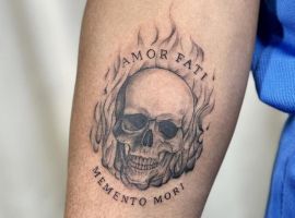 Модель з татуюванням "Amor Fati" на руці, що символізує прийняття долі та життєву філософію. Татуювання черепа з вогнем і написами "Amor Fati" та "Memento Mori".