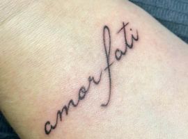 Маленьке тату "amorfati" на руці, виконане у стилі рукопису, символізує прийняття долі та життєвий філософський підхід. Тату "amorfati" на руці, стиль рукопису, символ прийняття долі.