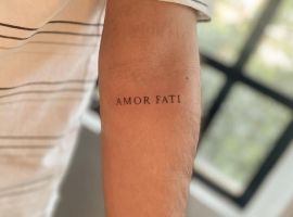 Маленьке тату "Amor Fati" на руці, що символізує прийняття життєвого шляху та філософію любові до своєї долі. Тату "Amor Fati" на передпліччі, символ прийняття долі.