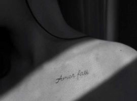 Малюнок тату "Amor Fati" на плечі, символ прийняття долі та філософії життя. Татуювання "Amor Fati" на плечі, чорний шрифт.