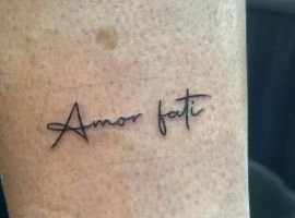 Модель з татуюванням "Amor Fati" у салоні Тату Cалон Альянс, що відображає ідею прийняття своєї долі та життєвого шляху. Татуювання "Amor Fati" на руці, створене в салоні Тату Cалон Альянс, символізує прийняття долі та жи.