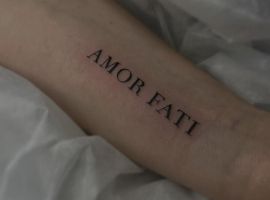 Модель з татуюванням "Amor Fati" на руці, символ прийняття долі та філософії життя. Татуювання "Amor Fati" на передпліччі, стильний дизайн.