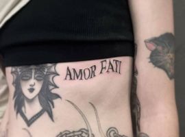 Татуювання "Amor Fati" на боці з жіночим портретом і ланцюгами, символізує прийняття долі та життєвий філософський підхід. Татуювання "Amor Fati" на боці з жіночим портретом і ланцюгами.