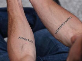 Мотиваційні татуювання "Amor Fati" і "Memento Mori" на передпліччях, символізують прийняття долі та життєвий шлях. Татуювання з цитатами "Amor Fati" та "Memento Mori" на передпліччях.